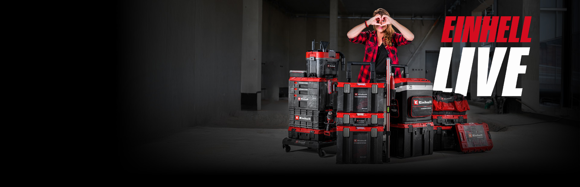 Person steht hinter gestapelten Einhell Werkzeugkoffern in Baustelle und formt Herz mit Händen, daneben Schriftzug „EINHELL LIVE“.