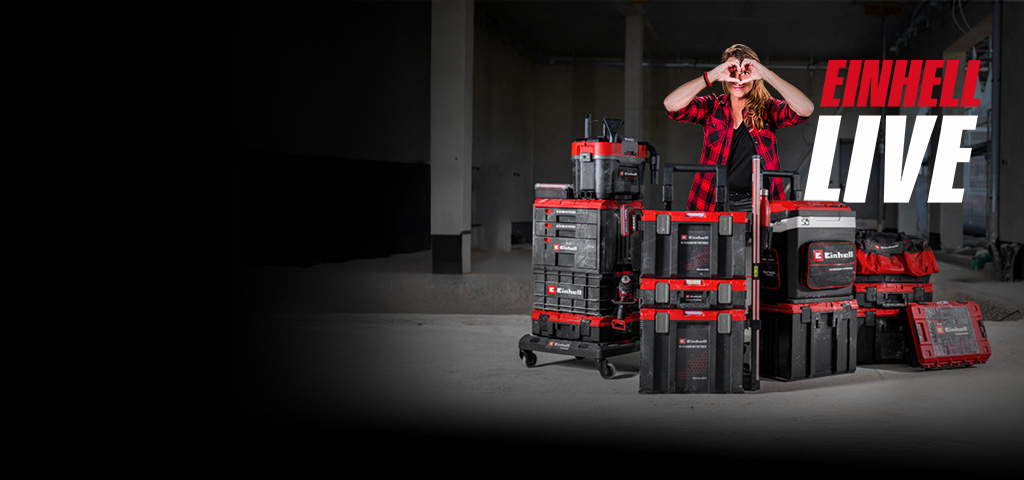 Person steht hinter gestapelten Einhell Werkzeugkoffern in Baustelle und formt Herz mit Händen, daneben Schriftzug „EINHELL LIVE“.
