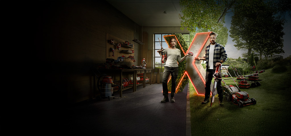 Two people stand in front of a large illuminated "X," surrounded by various cordless Einhell tools and garden equipment in a semi-open workshop and garden area.