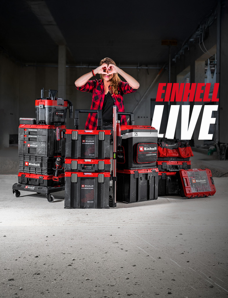 Person stands behind stacked Einhell tool cases on a construction site, making a heart with hands, next to the text “EINHELL LIVE”.