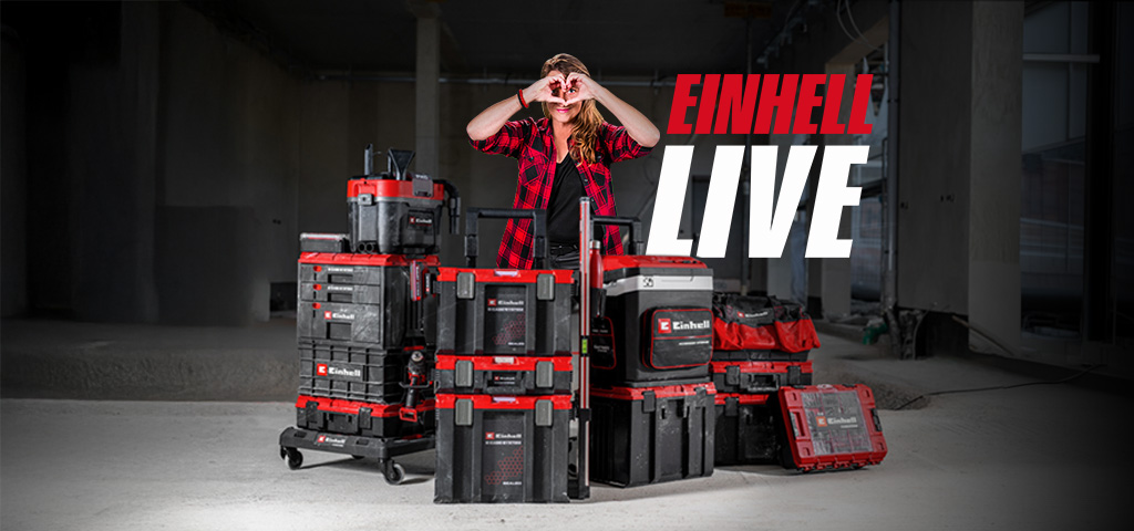 Person stands behind stacked Einhell tool cases on a construction site, making a heart with hands, next to the text “EINHELL LIVE”.