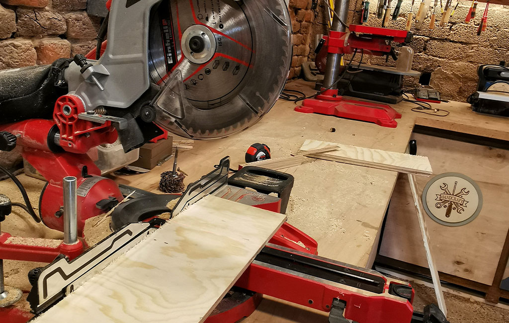 Eine Einhell Kappsäge schneidet eine Sperrholzplatte in einer Holzwerkstatt mit rotem Werkzeug auf der Werkbank.