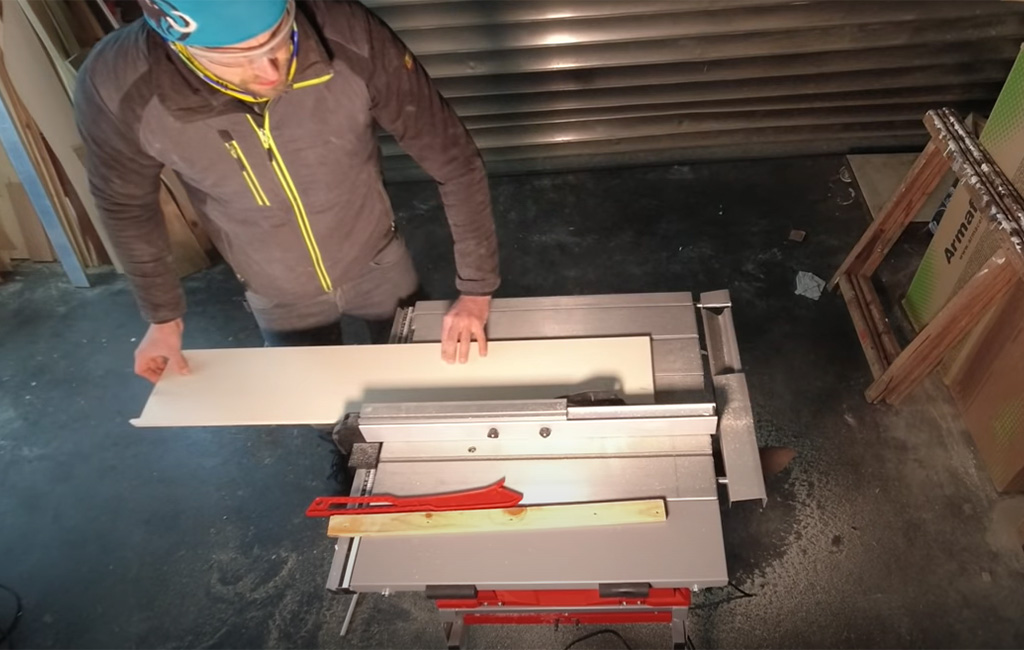 Mann schneidet eine Holzplatte mit einer Tischkreissäge in der Werkstatt zu.