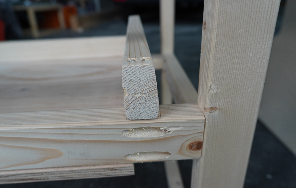 Detailaufnahme eines Holzrahmens mit eingefügtem Regalbrett und Taschenlochverbindungen.