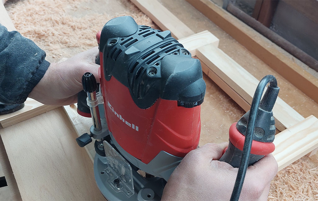 Eine Person arbeitet mit einer Einhell Oberfräse an einem Holzstück in einer Werkstatt.