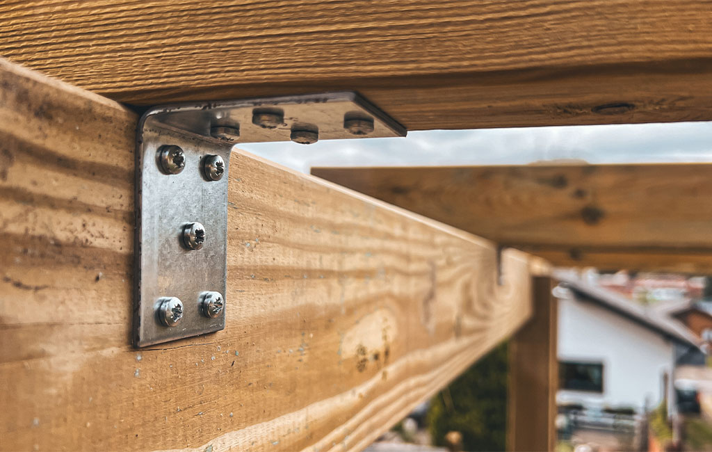 Nahaufnahme eines Metallwinkels mit Schrauben, der zwei Holzbalken verbindet.