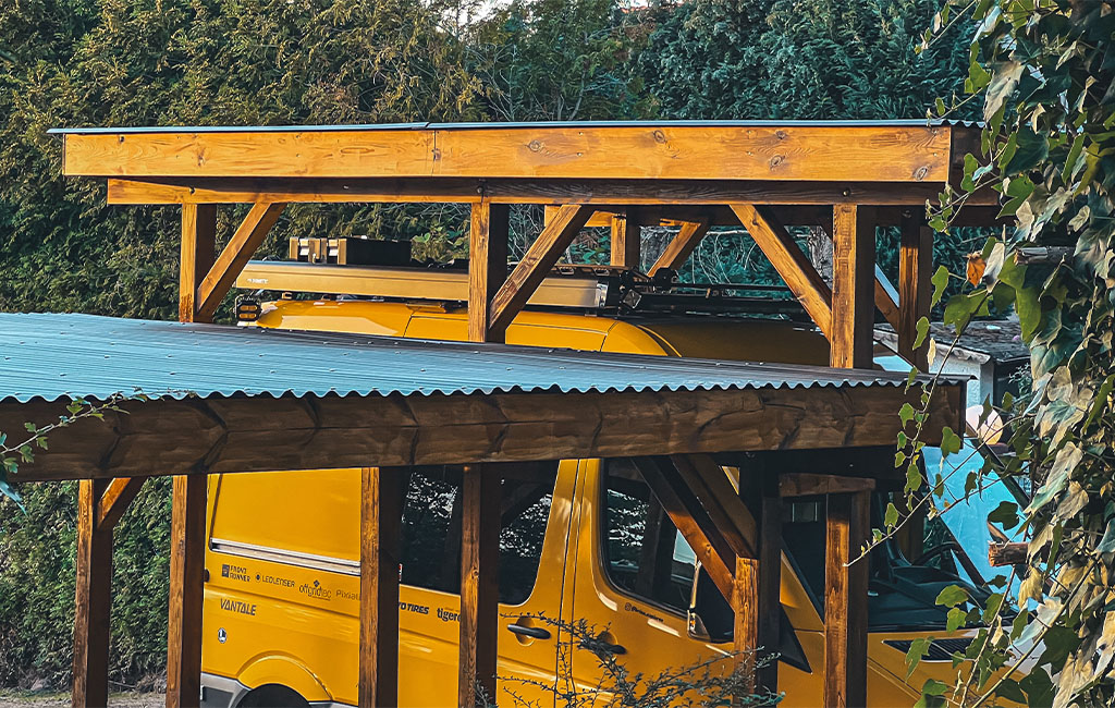 Nahaufnahme der Holzkonstruktion des Carports, im Hintergrund ein gelber Van.