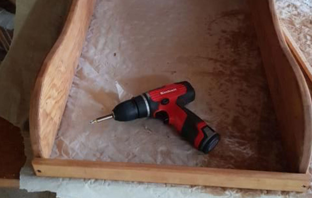 Ein roter Einhell Akku-Schrauber liegt in einem Holzrahmen auf einer Werkbank.