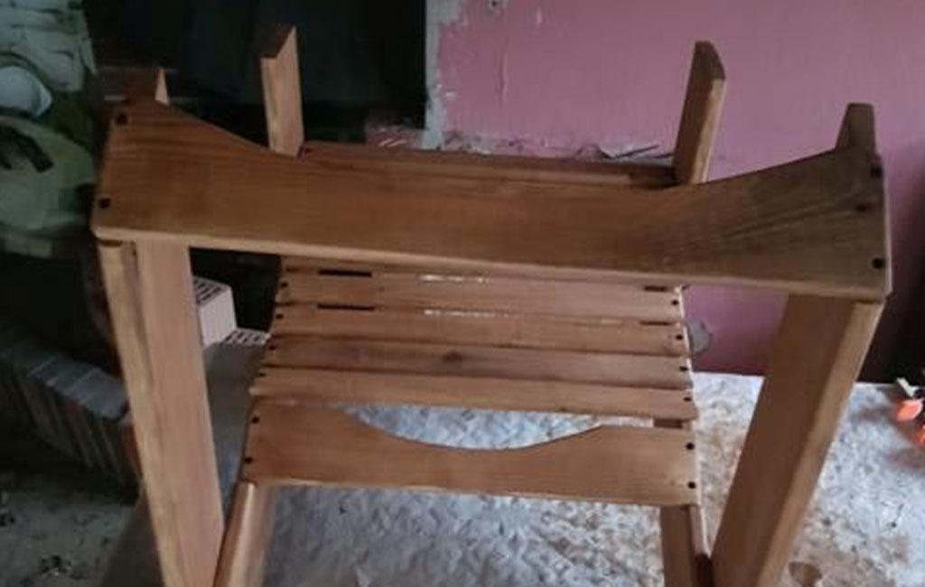 Der Rahmen eines Holzstuhls liegt auf dem Rücken, die Sitzfläche mit Latten ist von unten zu sehen.