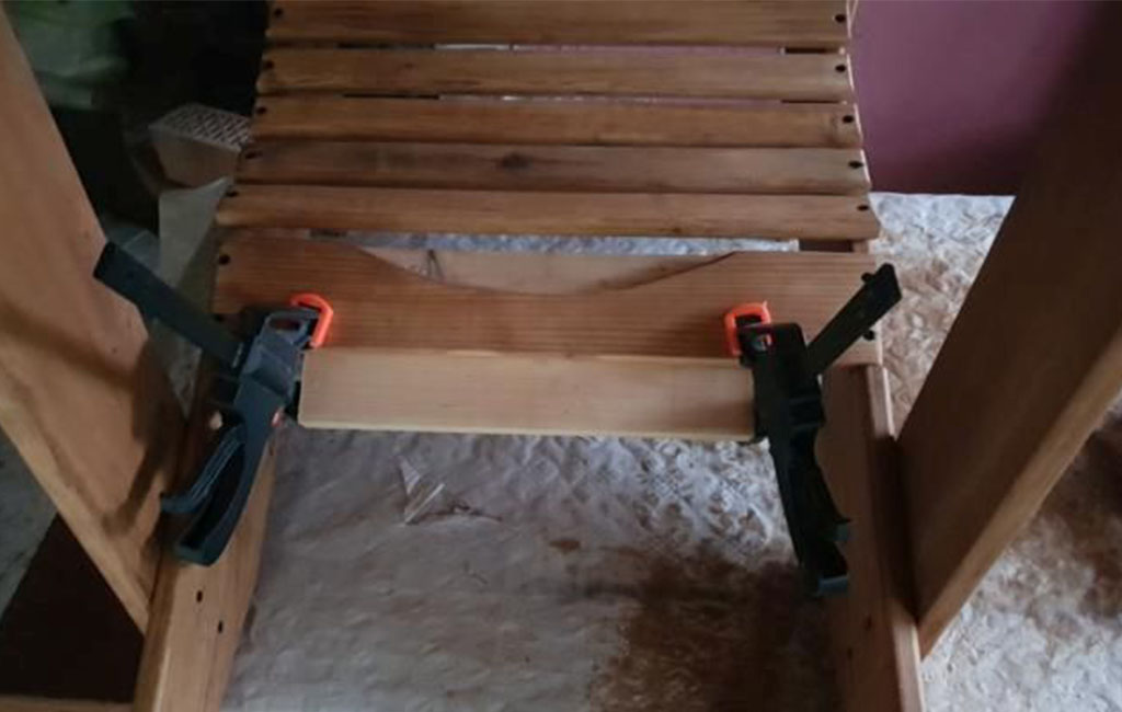 Eine Querlatte wird mit Schraubzwingen an den unteren Teil eines Holzstuhls montiert.
