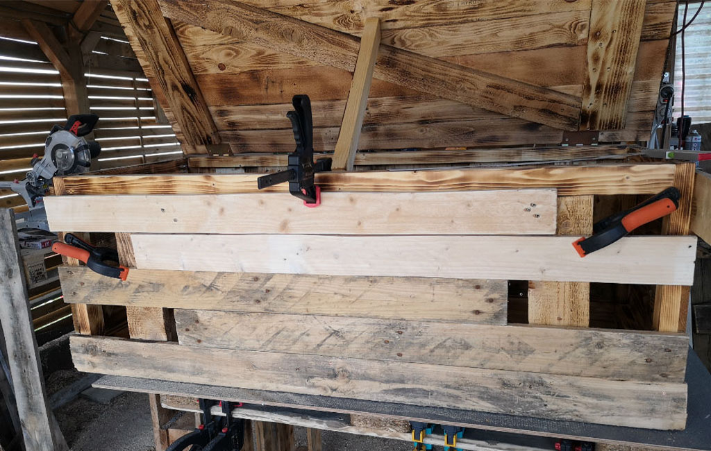 Eine Holztruhe im Bau. Mehrere Holzbretter sind mit Schraubzwingen an der Front befestigt.