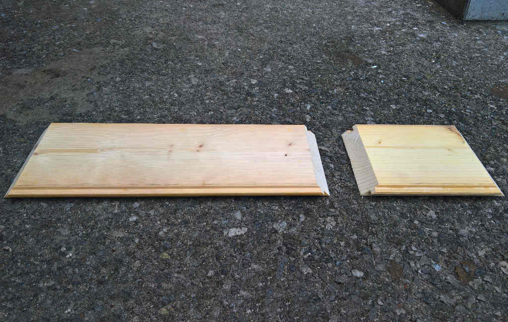Zwei zugeschnittene Holzbretter mit abgeschrägten Kanten liegen auf dem Boden.