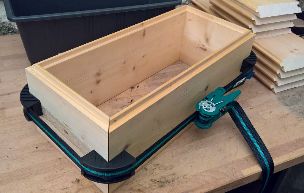 Ein rechteckiger Holzkasten mit Schraubzwingen wird auf einer Werkbank zusammengebaut.