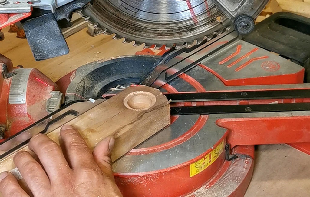 Eine Hand hält ein Holzstück mit runder Aussparung unter eine Kappsäge zur weiteren Bearbeitung.