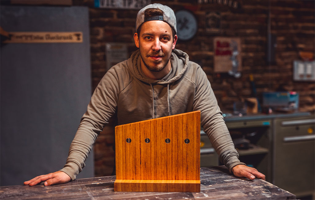 Ein Mann in grauem Hoodie präsentiert einen leeren Messerblock aus Holz mit vier Magnetpunkten auf der Rückseite.