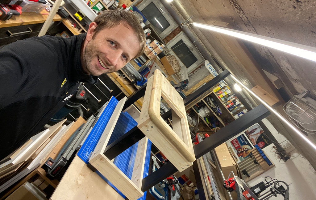 Ein Mann lächelt in die Kamera, während er an der Holzkonstruktion der Matschküche arbeitet.