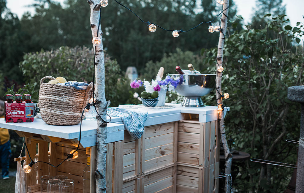 Rückseite der Bar mit Lichterkette, Getränken, Blumen und zwei Birkenstämmen als Deko.