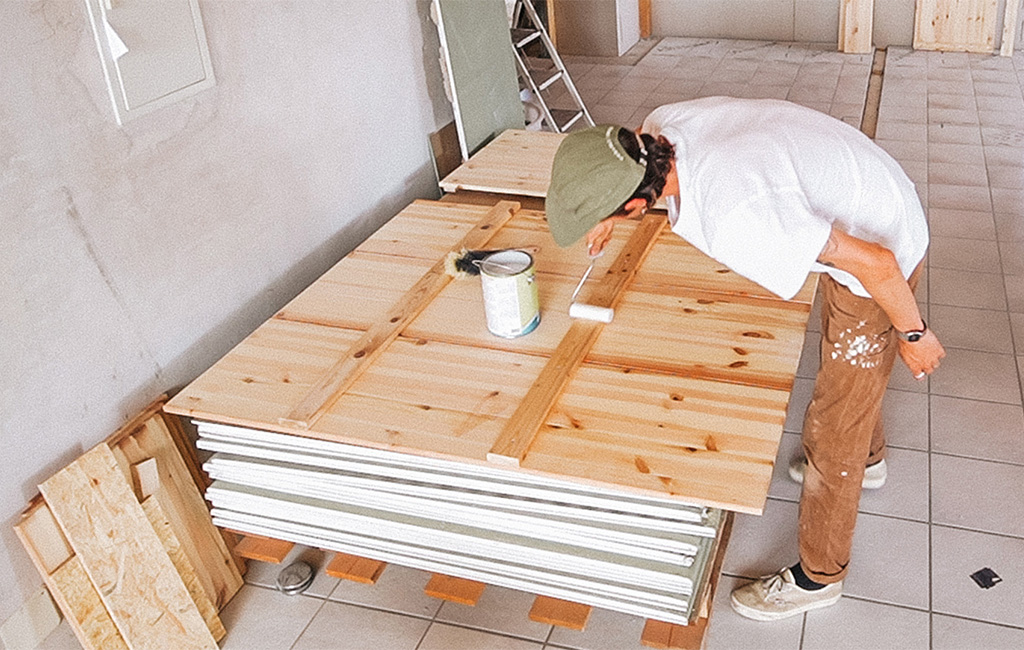 Ein Mann streicht Holzbretter für den Bau eines Strandkorbs aus Holz.