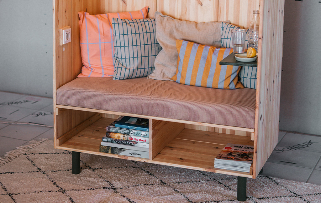 Detailaufnahme des Strandkorbs aus Holz mit Kissen, Ablage und Büchern im unteren Fach.